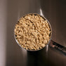 A metal measuring cup filled with Maia FLAKE™—a light, textured, flaked protein ingredient made from mushrooms and legumes, ideal for use in nuggets, seafood alternatives, and plant-based blends.
